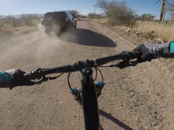 A photo of a mountain bike on a dusty road riding behind an SUV, taken from the bike rider's perspective.