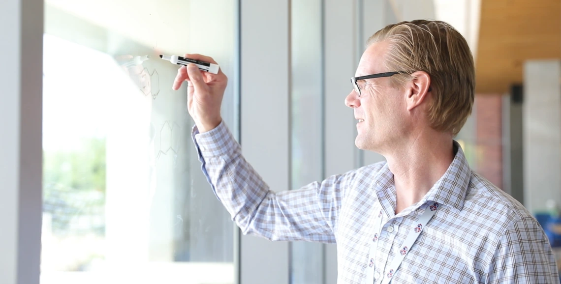 A man writing equations on glass