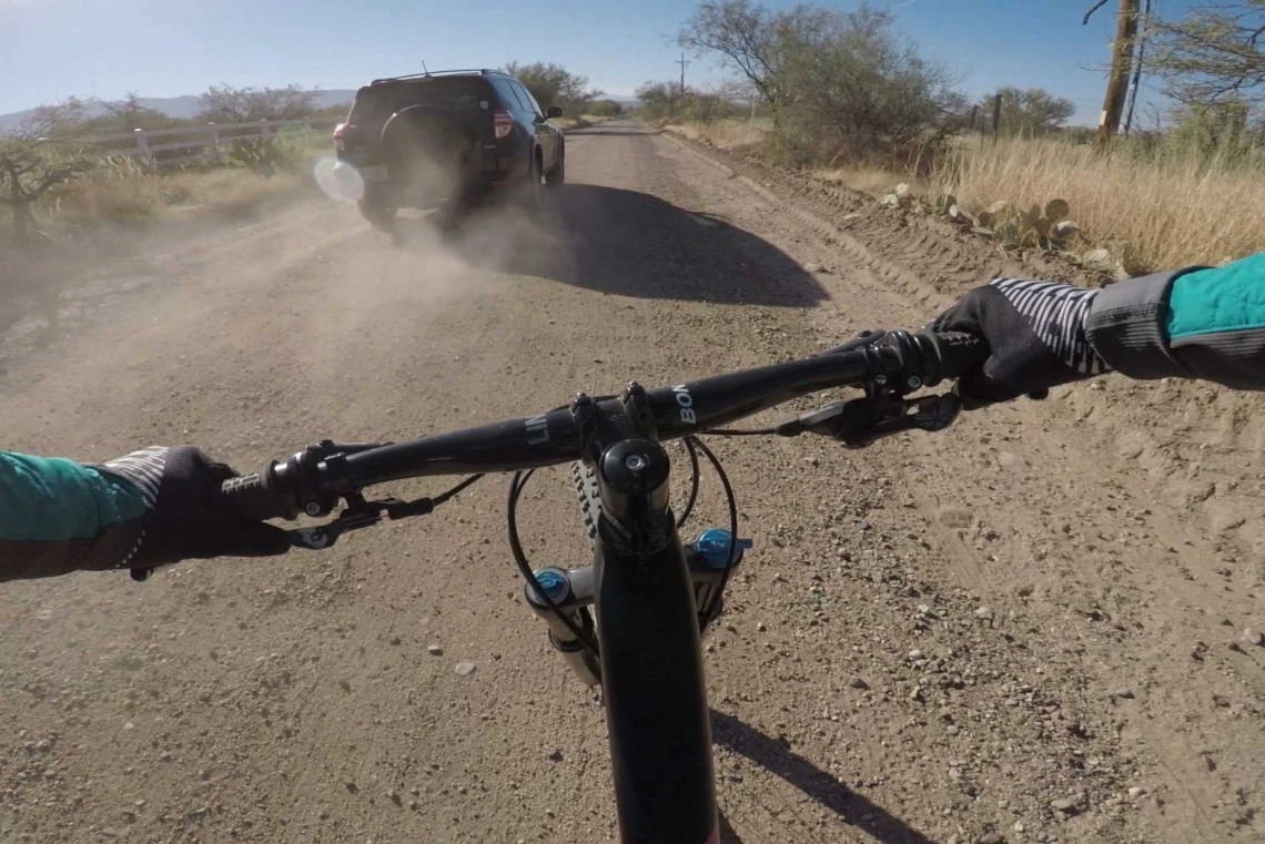 A photo of a mountain bike on a dusty road riding behind an SUV, taken from the bike rider's perspective.