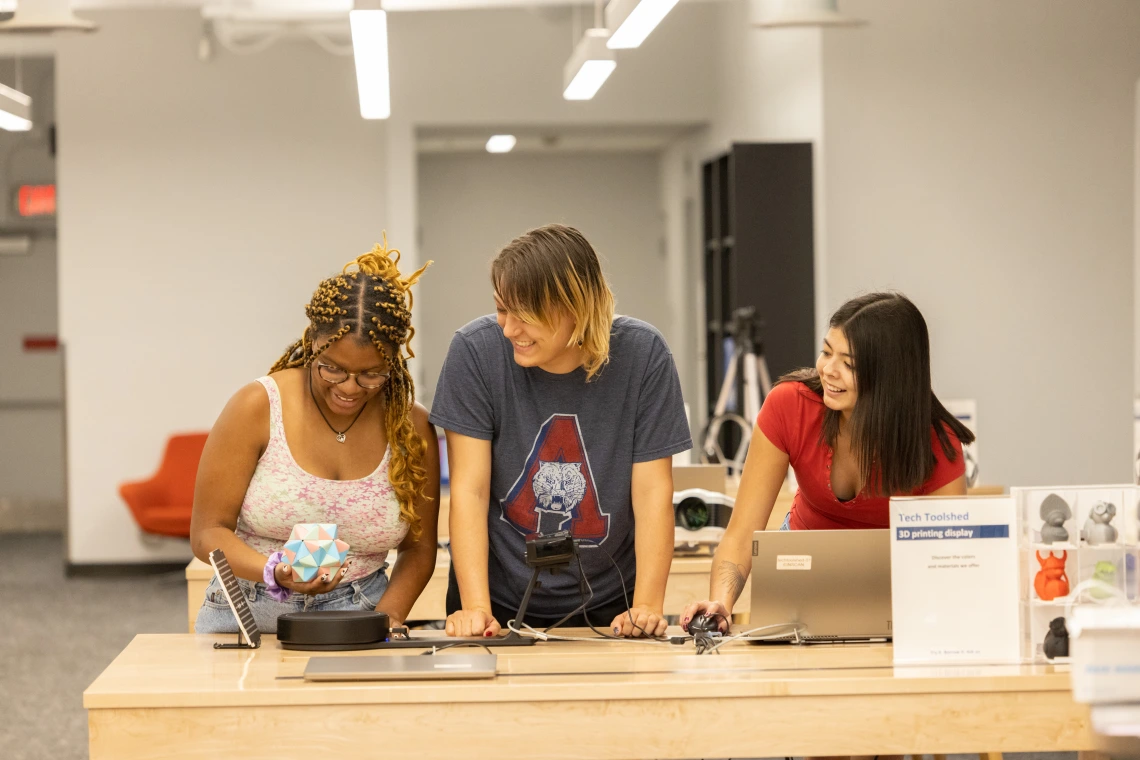 Three students looking at an invention at a desk.