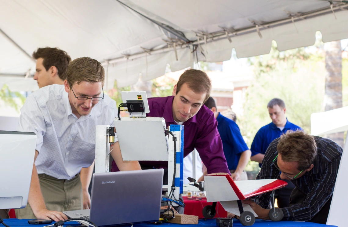 Three Inventors working on a computer at an outdoor table